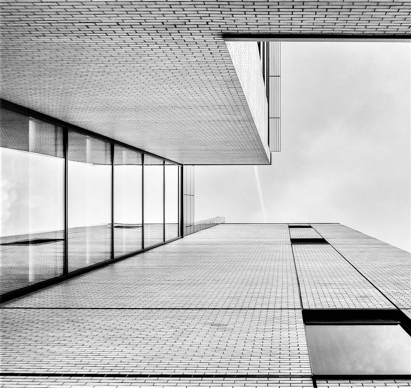 Blick nach oben entlang heller Klinkerfassaden mit Glasfront, Schwarz-Weiß-Architekturdetail – klare Linien als Sinnbild für den klaren Blick auf Ihre Immobilie